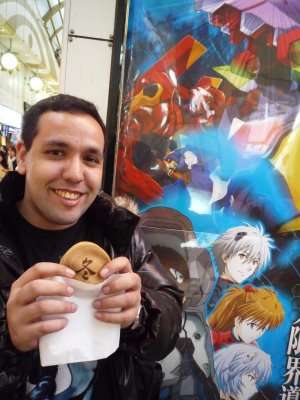 Visitante segurando um doce diante de um painel de Evangelion em Nakano