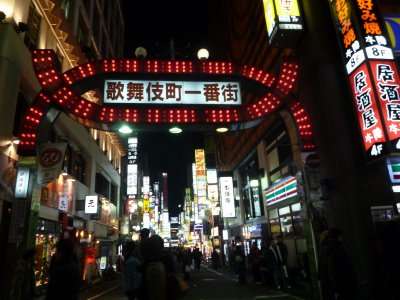 Entrada iluminada de Kabukichô à noite, com placas e pedestres