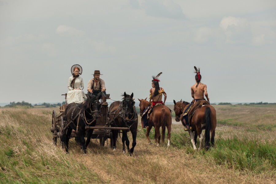 "People in a wagon pass people on horseback. "